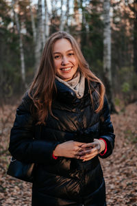 Portrait of young woman standing against trees