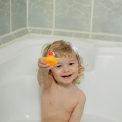 Portrait of smiling boy with arms raised in bathroom