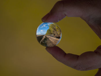 Close-up of hand holding crystal ball against sky