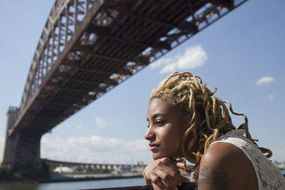 Side profile of a young woman beneath a bridge