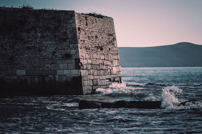 Stone wall by sea against clear sky