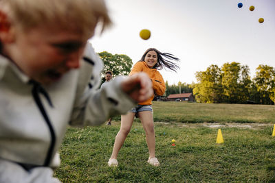 Smiling girl throwing ball on friend while playing in playground at summer camp