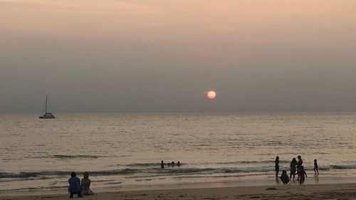 People at beach against sky during sunset