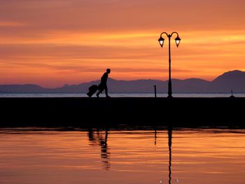 Silhouette man walking on pier over lake against orange sky