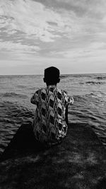 Rear view of man looking at sea while sitting against sky