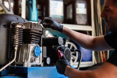 Side view of professional mechanic in protective gloves inspecting engine while working in repair service workshop