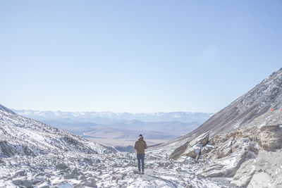 Rear view of man standing on snowcapped mountain against sky