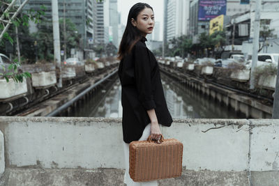 Portrait of young woman standing by railing in city