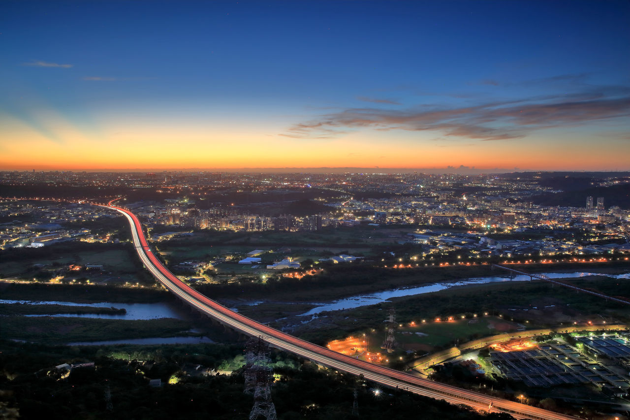 HIGH ANGLE VIEW OF ILLUMINATED CITY AGAINST SKY AT NIGHT