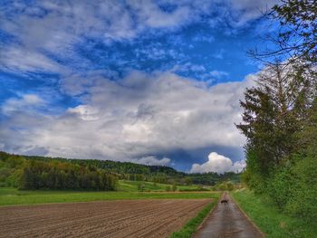 Empty road amidst field against sky