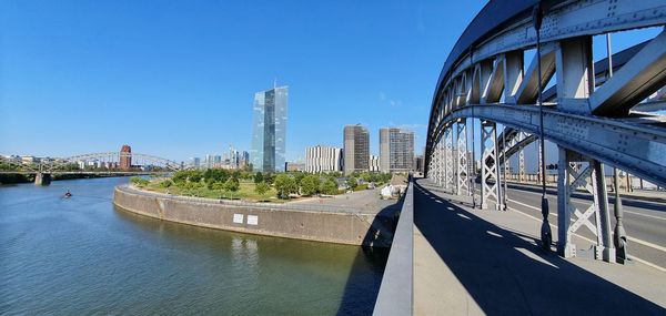 Bridge over river in city against clear blue sky