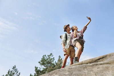 Low angle view of happy friends taking selfie against sky