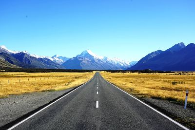 Road leading towards mountains against blue sky