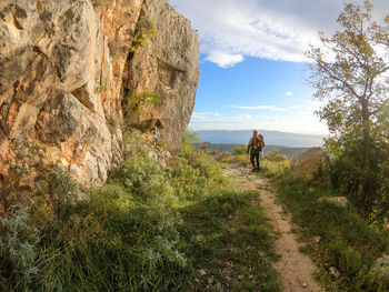 Rear view of man hiking on mountain against cloudy sky