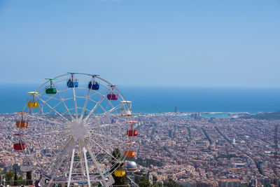 Ferris wheel by sea against sky in city