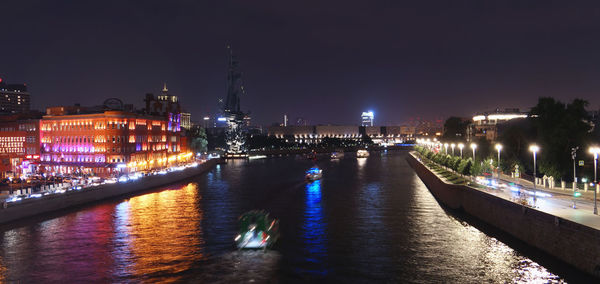 Illuminated bridge over river amidst buildings in city at night