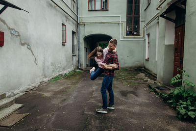 Cheerful man carrying woman while standing on footpath