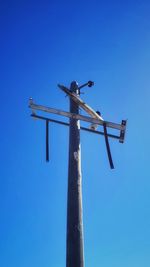 Low angle view of bird perching on wooden post against clear blue sky