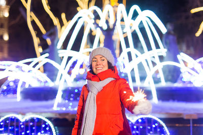 Portrait of smiling young woman standing in city at night