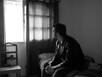 Side view of man sitting on bed looking out the window