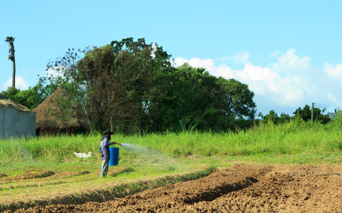 Farmer spraying fertilizer on field against sky