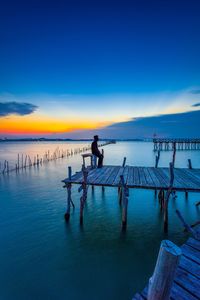 Silhouette man standing on pier by sea against sky during sunset