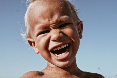 Close-up portrait of boy with mouth open against sky