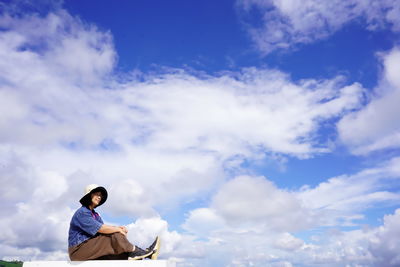 Low angle view of man sitting against sky