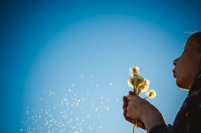 Woman blowing dandelion while standing against sky