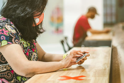 Midsection of woman holding mobile phone while sitting on table