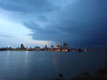 Sea by illuminated city against sky at dusk