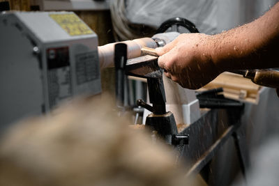 A man in a working apron works on a wood turning lathe. hands hold a chisel. hobby