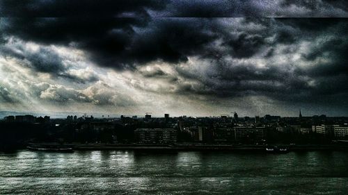 View of city at waterfront against cloudy sky