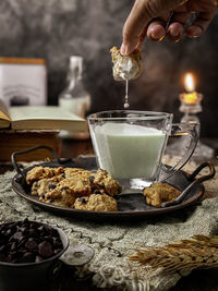 Cropped hand of person dipping a cookies in a glass of milk on table