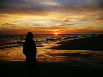 Rear view of man standing on beach against sunset sky