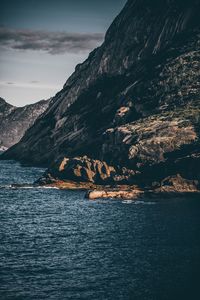 Scenic view of sea by mountain against sky