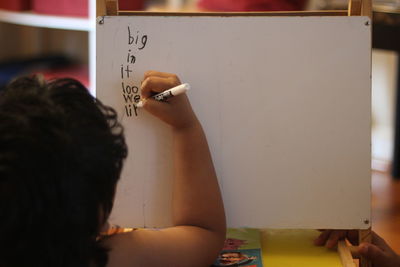 Rear view of girl writing on board