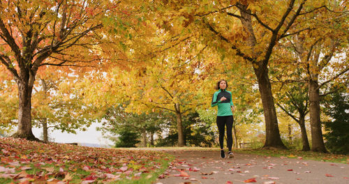 Young woman on running amidst autumn trees