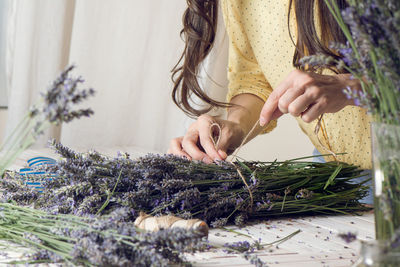 Midsection of florist arranging bunch of lavender flowers on table