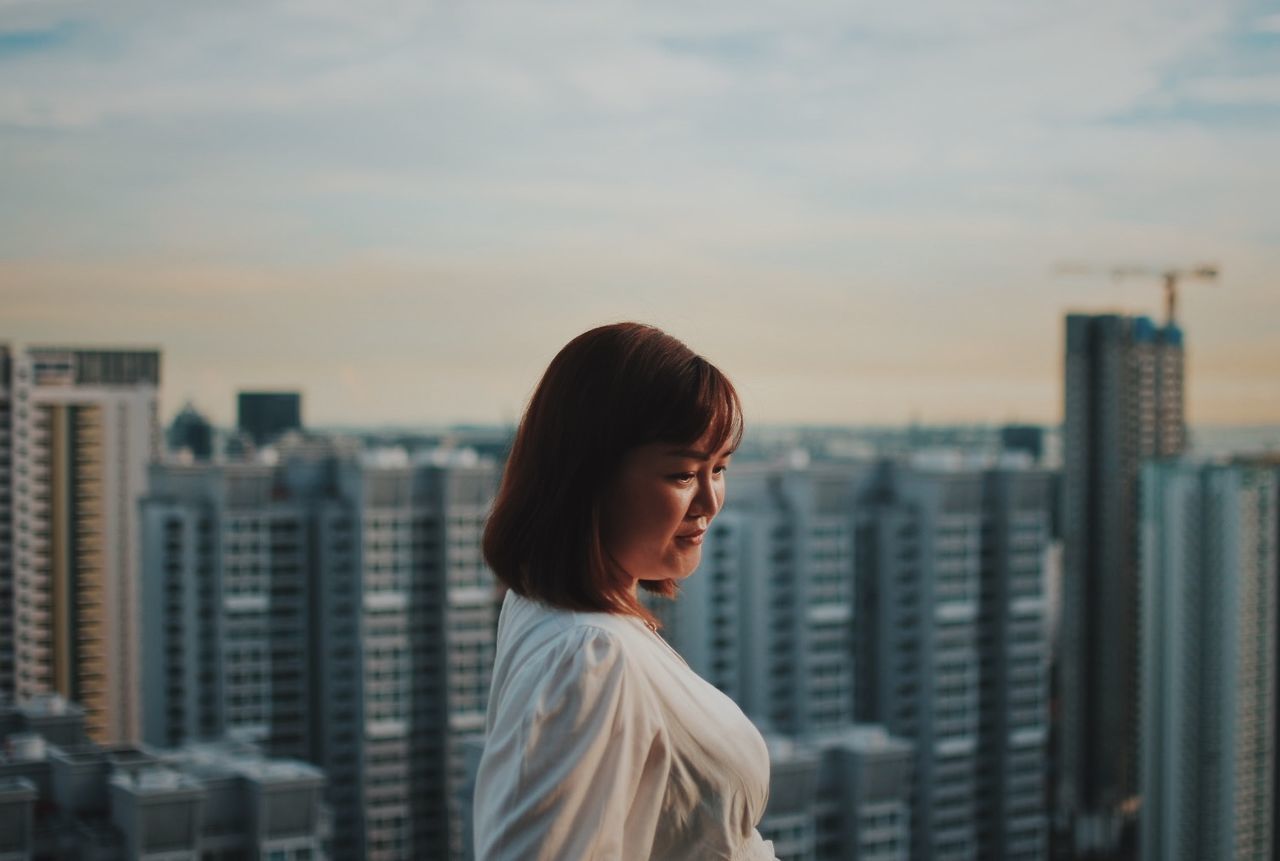 PORTRAIT OF WOMAN LOOKING AT CITY BUILDINGS