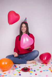 Smiling young woman holding balloons against wall against gray background