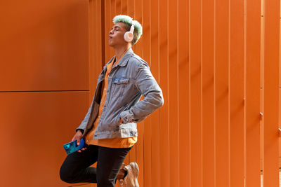 Young woman looking away while standing against orange wall