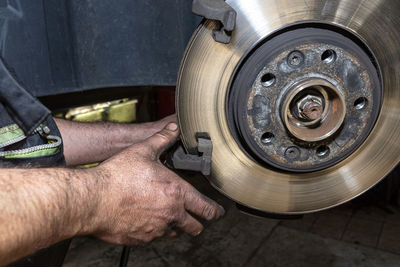 A car mechanic pulls a brake caliper in a car standing on a car jack in the workshop.