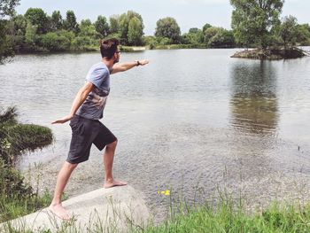 Side view of young man standing on rock by lake