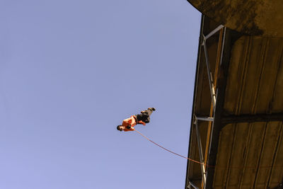 Low angle view of man rappelling against clear sky