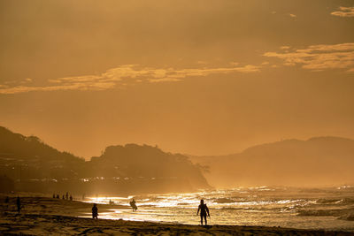 Silhouette people on beach against sky during sunrise