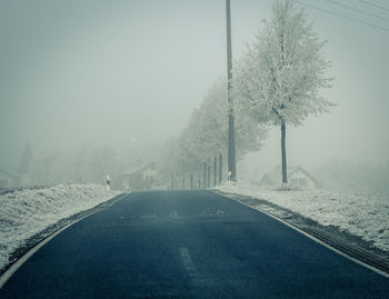 Road amidst trees against sky during foggy weather