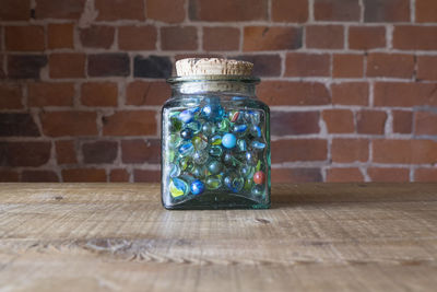 Marbles in glass jar on table against brick wall