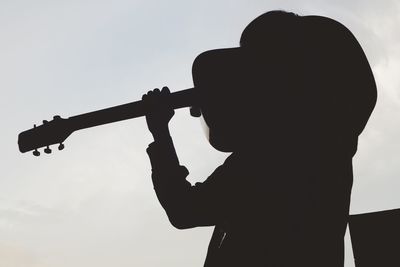Low angle view of silhouette man holding camera against sky
