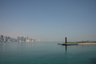 Sea and buildings in city against clear sky